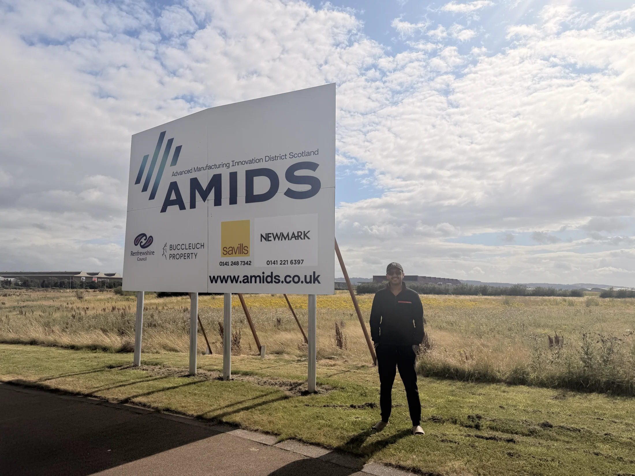 Varun Sharma beside an AMIDS sign during a wider-area visit on 1 August 2026